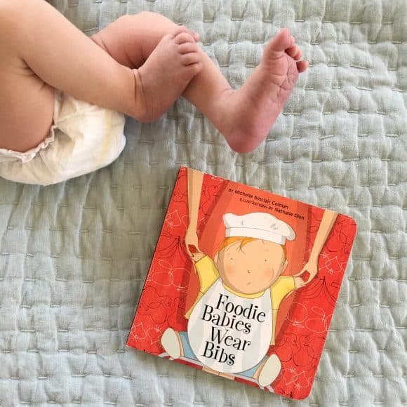 Baby's legs and a book about kids and eating on a bed