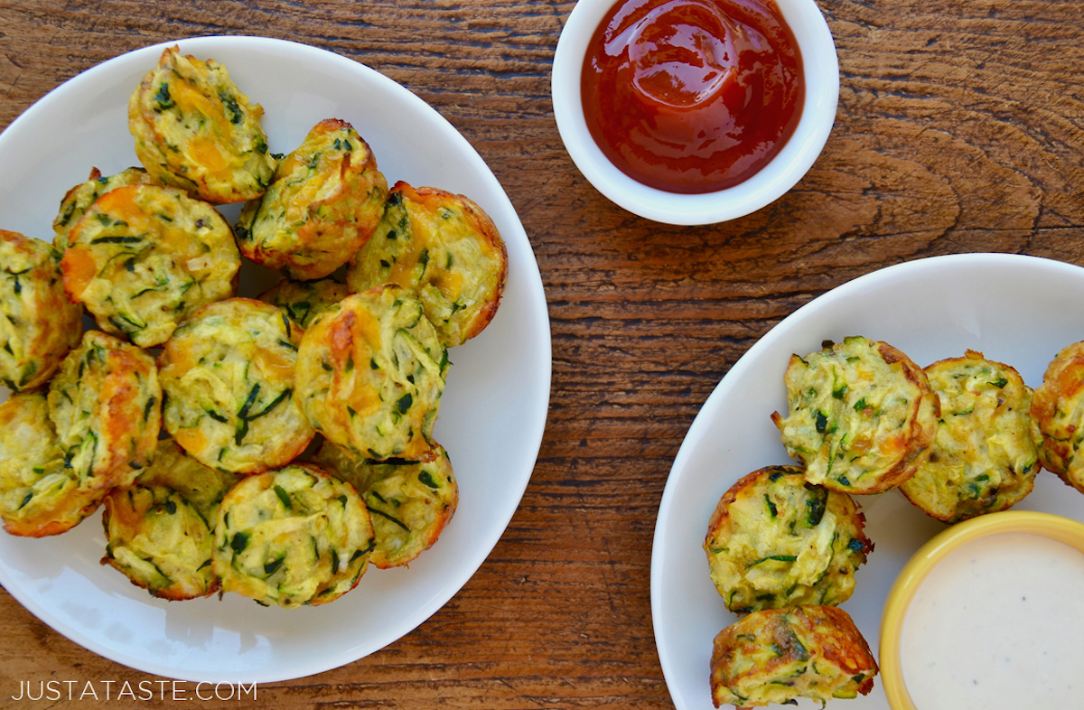 Cheesy zucchini tots on a white plate next to a small white ramekin containing ketchup.