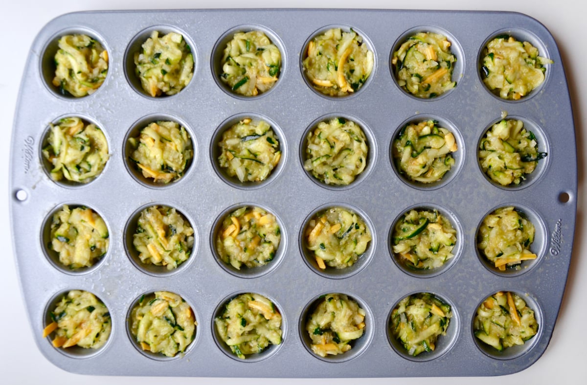 A mini muffin pan containing zucchini tot batter.