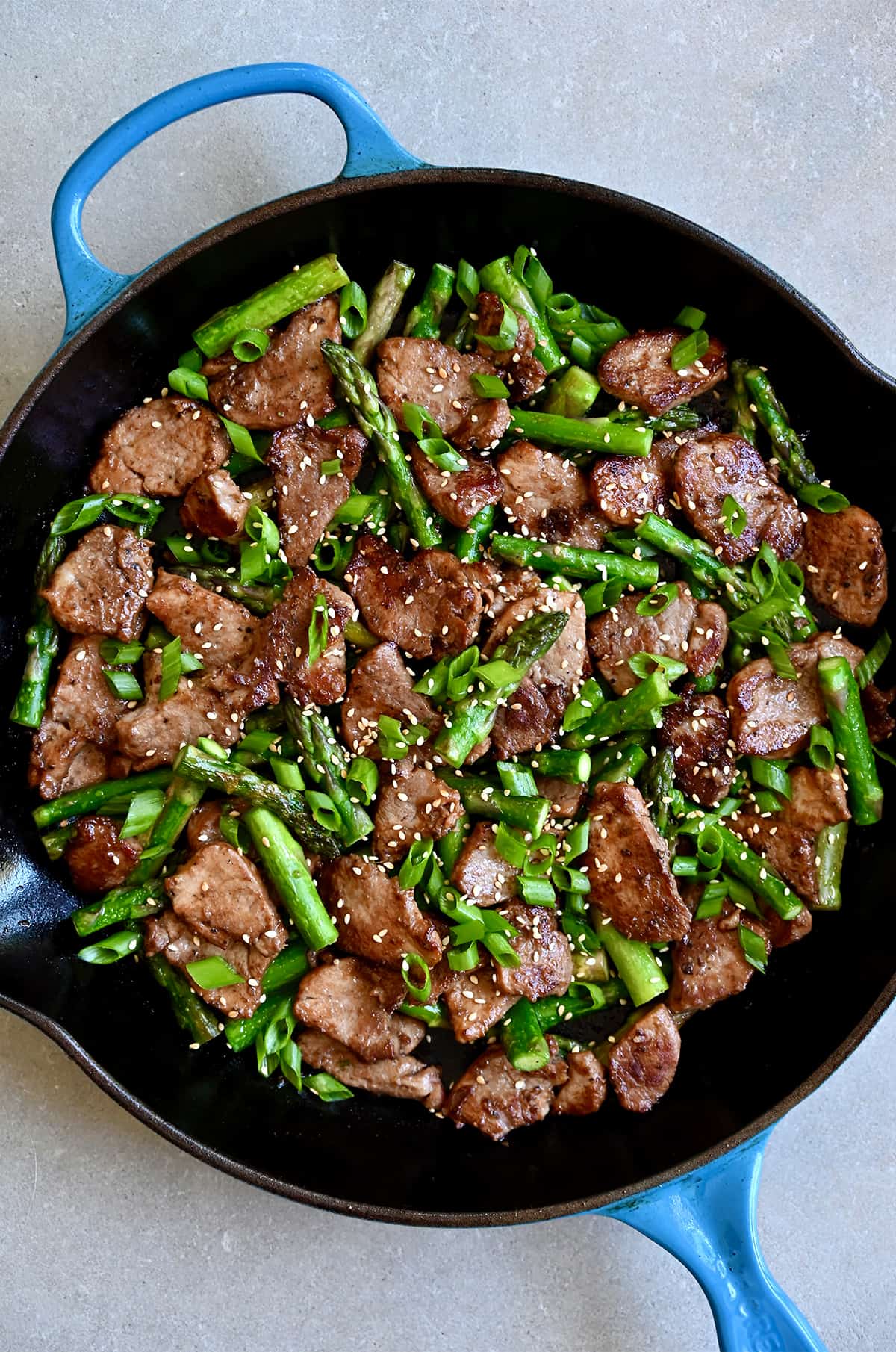 Black pepper pork and asparagus in a skillet and garnished with toasted sesame seeds and sliced scallions.
