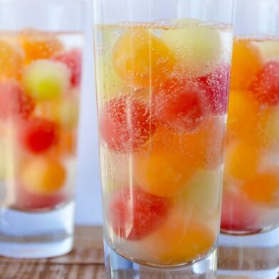 Three clear cocktail glasses containing melon balls and soda water