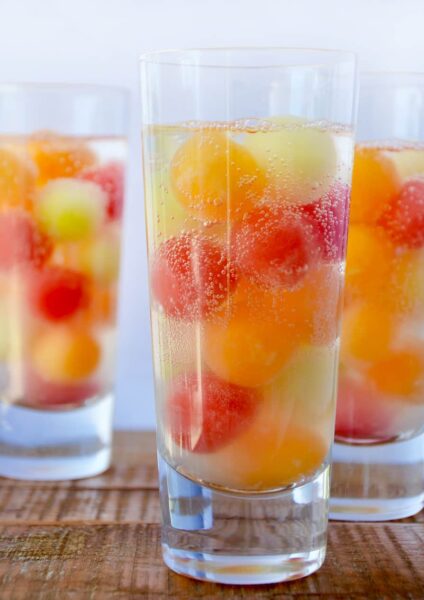 Three clear cocktail glasses containing melon balls and soda water