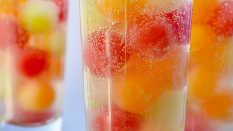 Three clear cocktail glasses containing melon balls and soda water