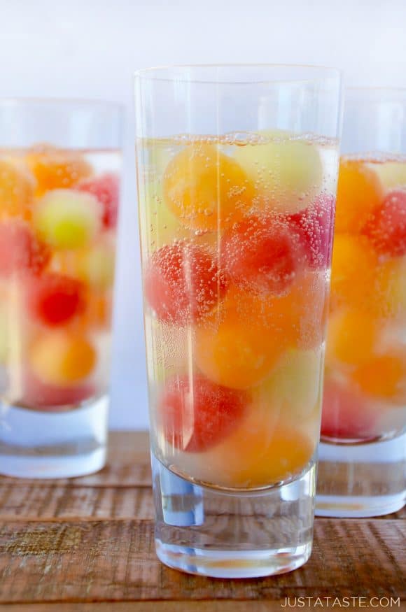 Three clear cocktail glasses containing melon balls and soda water