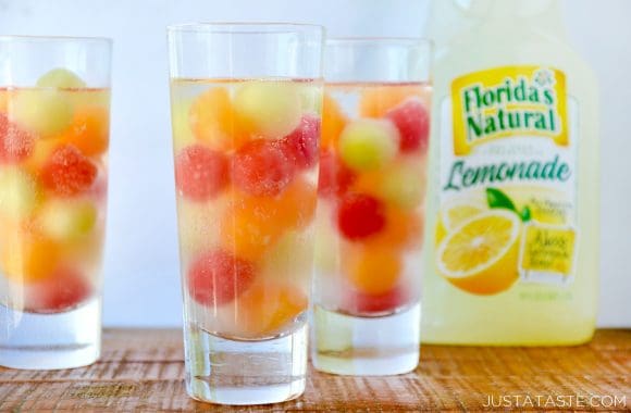 Three clear cocktail glasses containing melon balls with a jug of lemonade