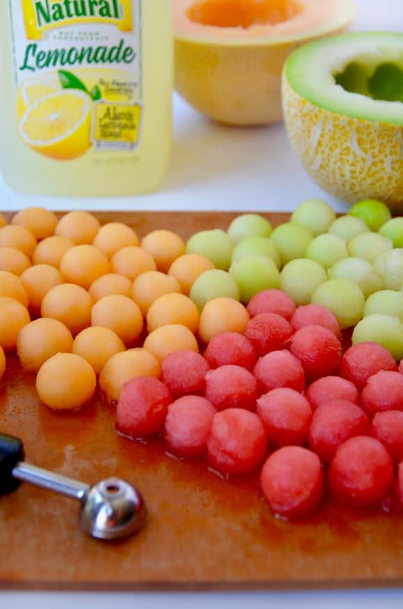 Melon balls on a cutting board with lemonade in the background