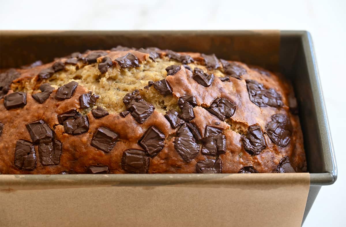 Golden-brown banana bread studded with chocolate chunks in a parchment paper-lined bread pan.