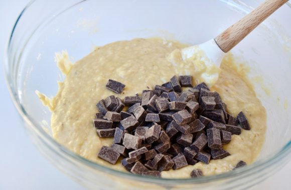 One-bowl banana bread mixture in clear bowl with chocolate chunks and spatula