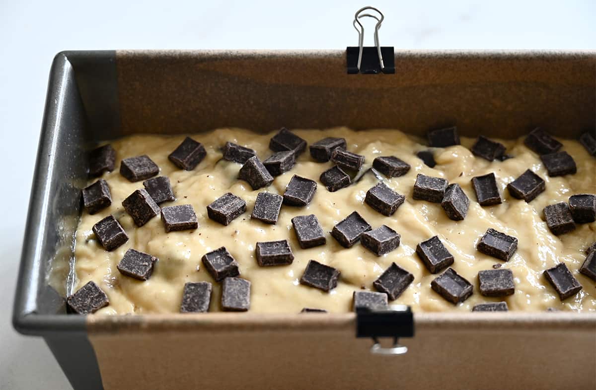 A parchment paper-lined bread pan containing banana bread batter topped with chocolate chunks.