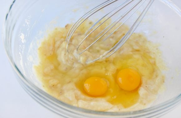 Clear bowl with mashed bananas and two eggs with whisk