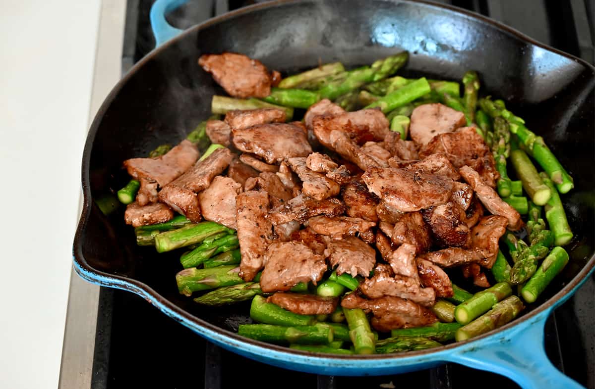 Stir-fried pepper pork and asparagus pieces in a large skillet.