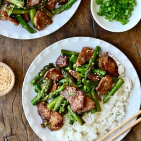Quick black pepper pork with asparagus atop steamed white rice on a plate with chopsticks.