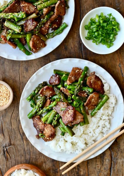 Quick black pepper pork with asparagus atop steamed white rice on a plate with chopsticks.