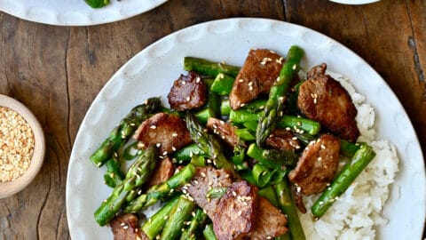 Quick black pepper pork with asparagus atop steamed white rice on a plate with chopsticks.