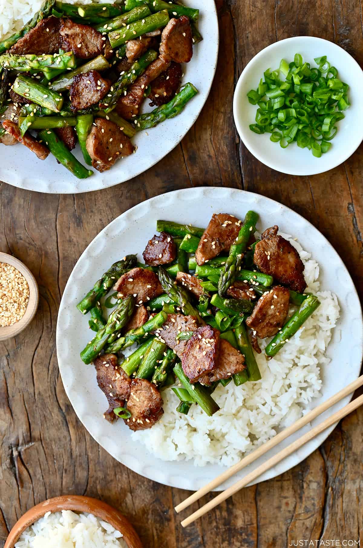 Quick black pepper pork with asparagus atop steamed white rice on a plate with chopsticks.