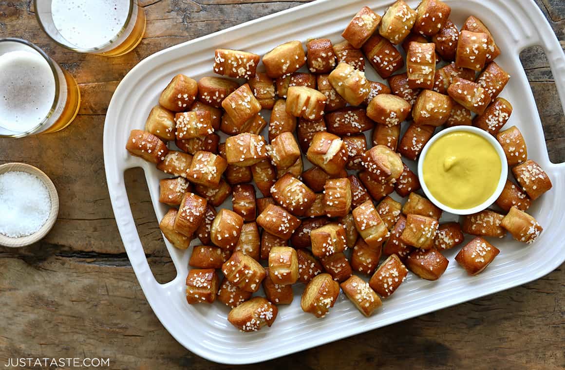 Glasses of beer next to a serving platter containing the best homemade soft pretzel bites and a small ramekin filled with yellow mustard