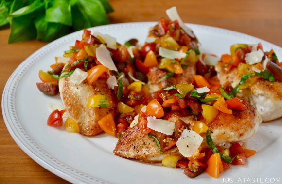 A white plate containing chicken breasts topped with chopped tomatoes, basil and Parmesan cheese shavings