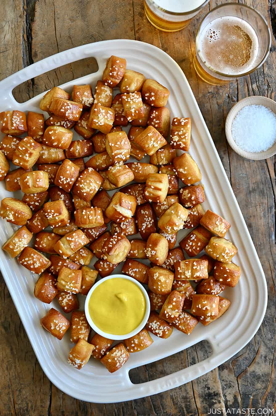 A top-down view of a white serving platter piled high with pretzel bites and a ramekin filled with yellow mustard