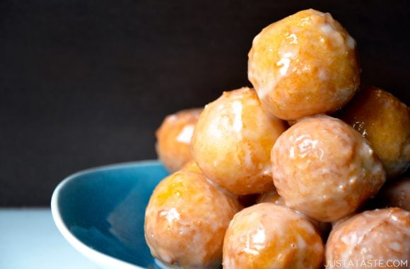 A blue bowl containing homemade glazed doughnut holes stacked on top of each other