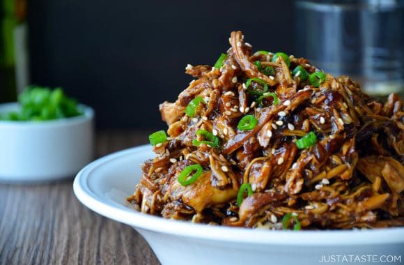 A white bowl containing shredded chicken topped with scallions and sesame seeds