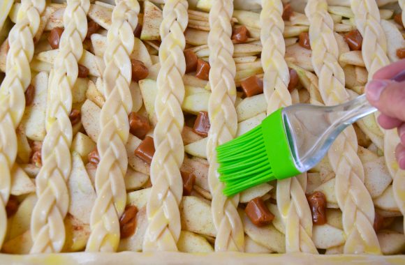 An unbaked caramel apple slab pie being brushed with eggwash