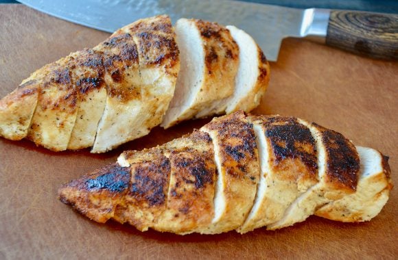 Two sliced chicken breasts on cutting board with knife