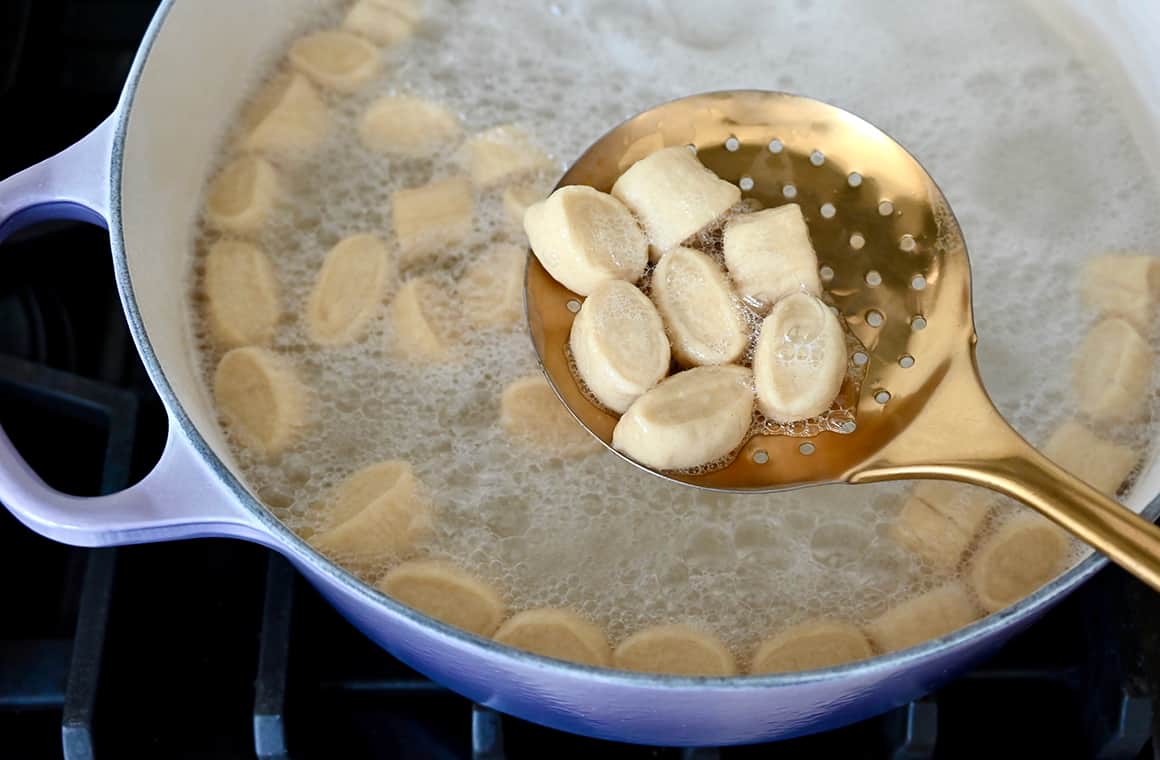 A top-down view of a slotted spoon with dough over a pot containing baking soda and water