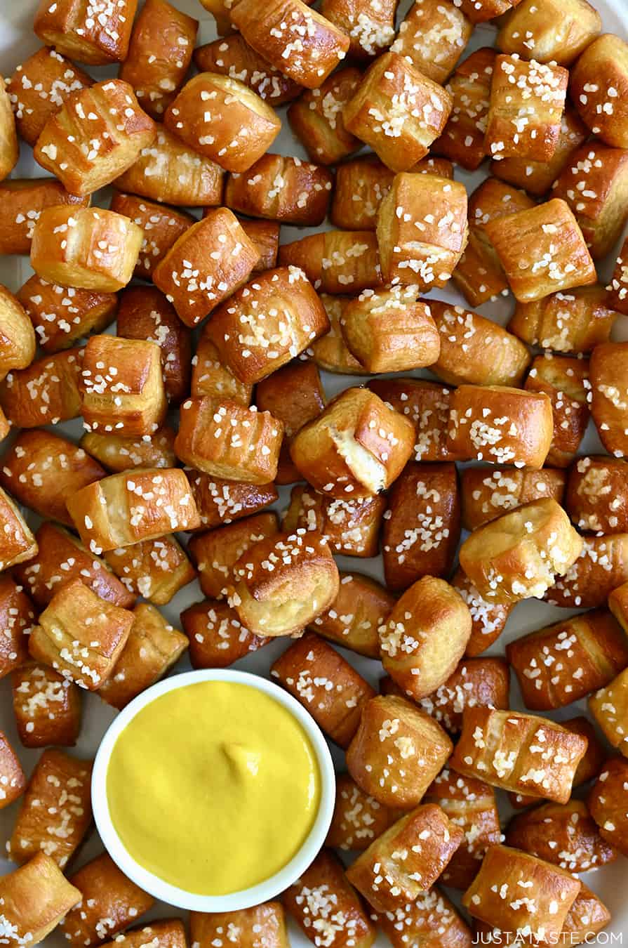 Una vista ravvicinata di morsi di pretzel morbidi fatti in casa che circondano un piccolo ramekin ripieno di senape gialla