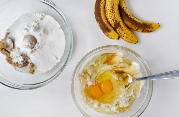 Overripe bananas and two bowls with wet and dry ingredients for Sour Cream Chocolate Chunk Banana Bread