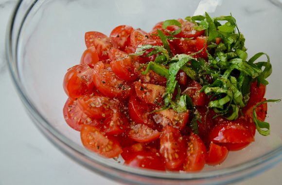 Bowl containing cherry tomato salad with fresh basil and cracked pepper