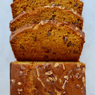A loaf of pumpkin bread topped with pecans with four pieces sliced off of it.