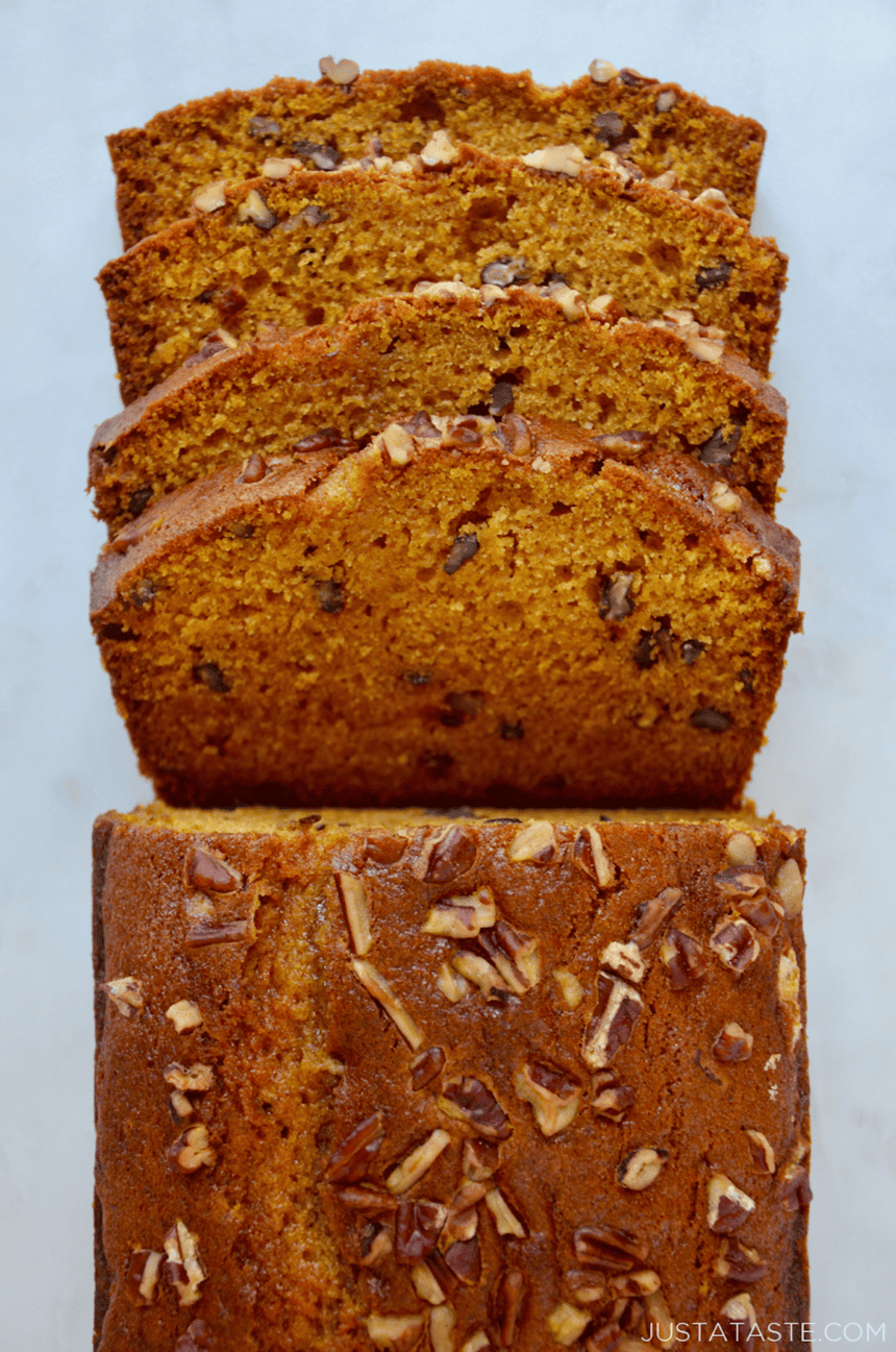A loaf of pumpkin bread topped with pecans with four pieces sliced off of it.