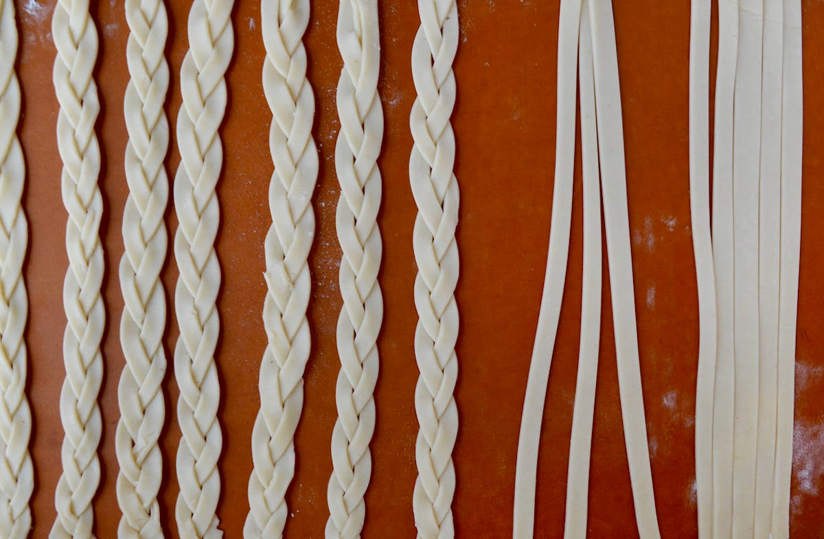 A cutting board with pie dough that has been cut into three long 1/2-inch strips and pie dough that has been braided into five braids for the lattice top.
