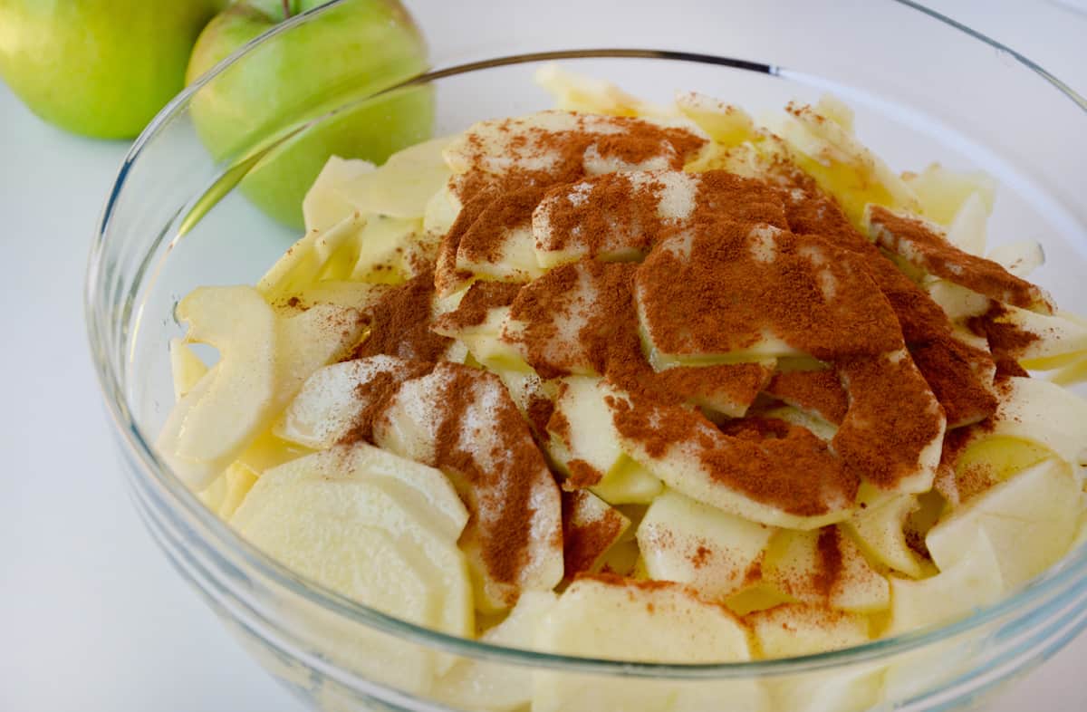 A medium glass bowl with apples, sugar, cornstarch, cinnamon and lemon juice.