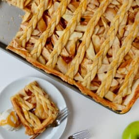 A sheet pan with caramel apple slab pie with a lattice topping next to a plate with a slice of pie and a scoop of vanilla ice cream.