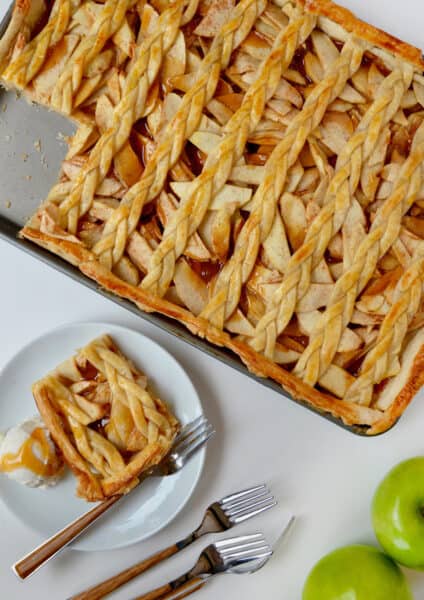 A sheet pan with caramel apple slab pie with a lattice topping next to a plate with a slice of pie and a scoop of vanilla ice cream.