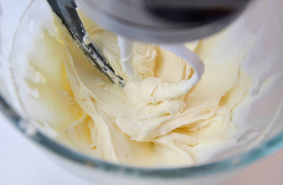 In the bowl of a stand mixer, cream cheese frosting is being mixed with the paddle attachment.