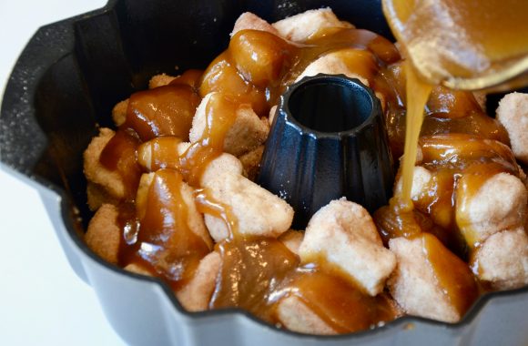 Butter mixture being poured on top of monkey bread pieces in bundt pan