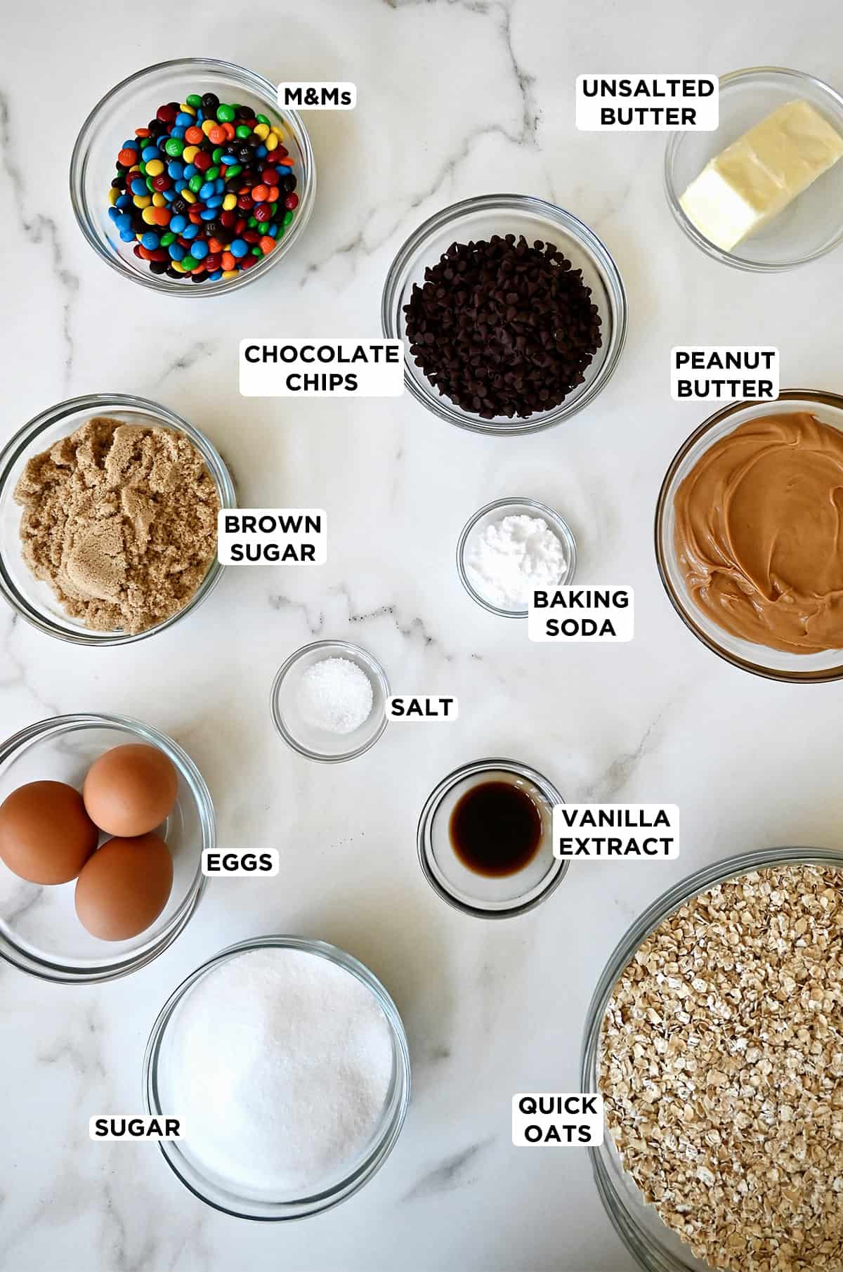 Ingredients to make monster cookies in various sizes of glass bowls.