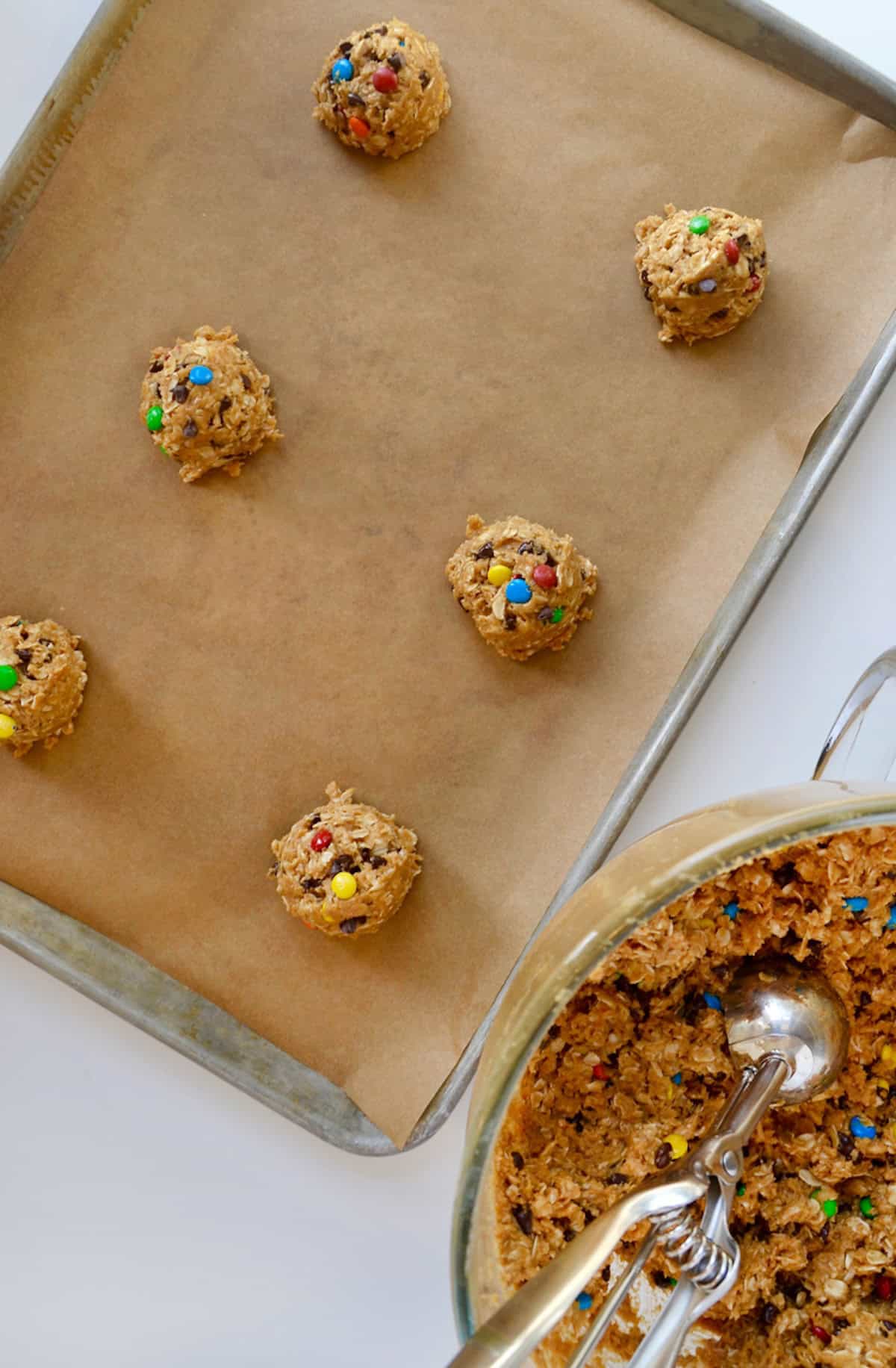 Mounds of monster cookie dough on a parchment paper-lined cookie sheet.