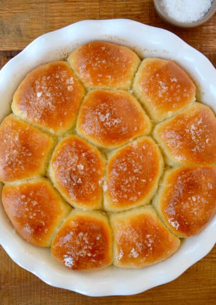 Freshly baked soft dinner rolls garnished with large-flake sea salt in a white round baking dish.