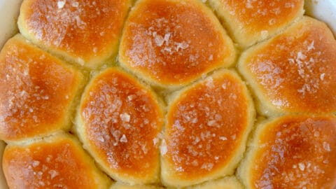 Freshly baked soft dinner rolls garnished with large-flake sea salt in a white round baking dish.