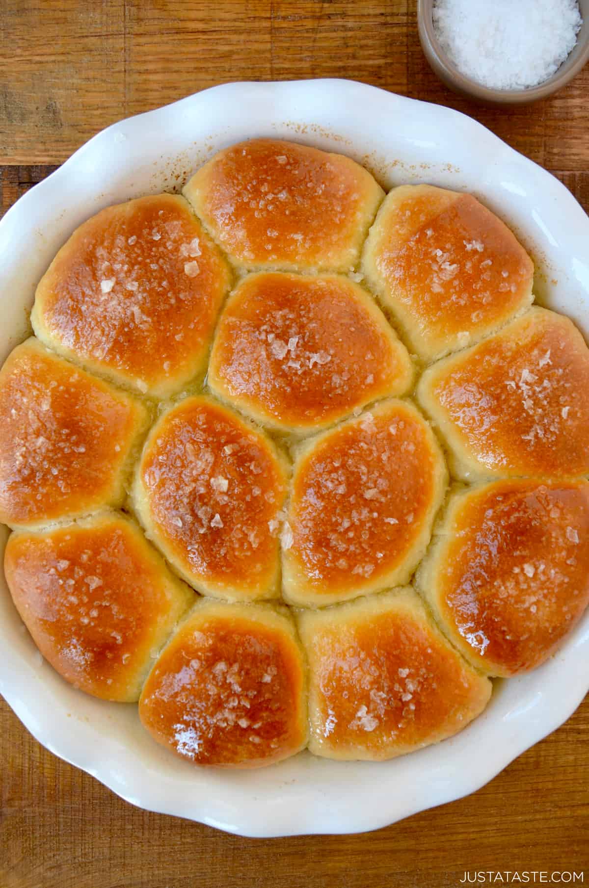 Freshly baked soft dinner rolls garnished with large-flake sea salt in a white round baking dish.