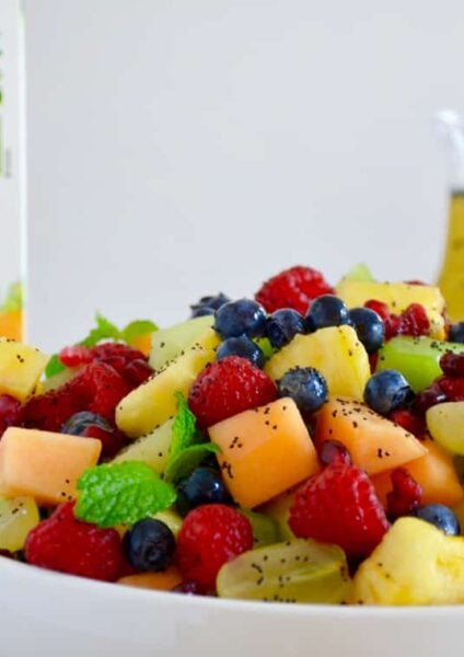 A white bowl with fruit salad and a carton of orange juice in the back