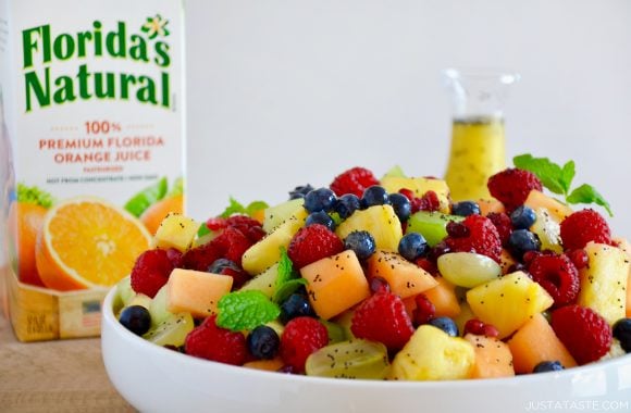 A white bowl with fruit salad and a carton of orange juice in the back