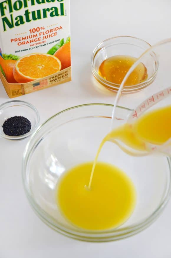 A glass bowl with orange juice being poured into it