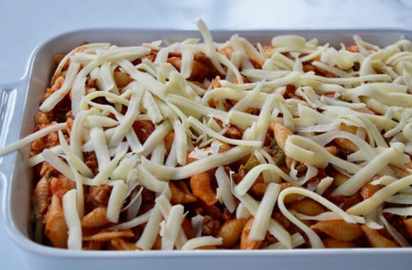 Unbaked pizza pasta in white baking dish topped with shredded cheese