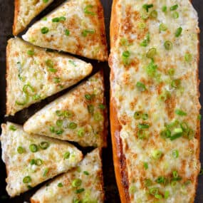 Two cheesy garlic bread loafs topped with sliced scallions.