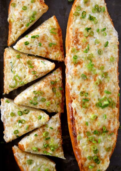 Two cheesy garlic bread loafs topped with sliced scallions.