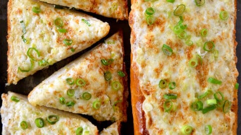 Two cheesy garlic bread loafs topped with sliced scallions.